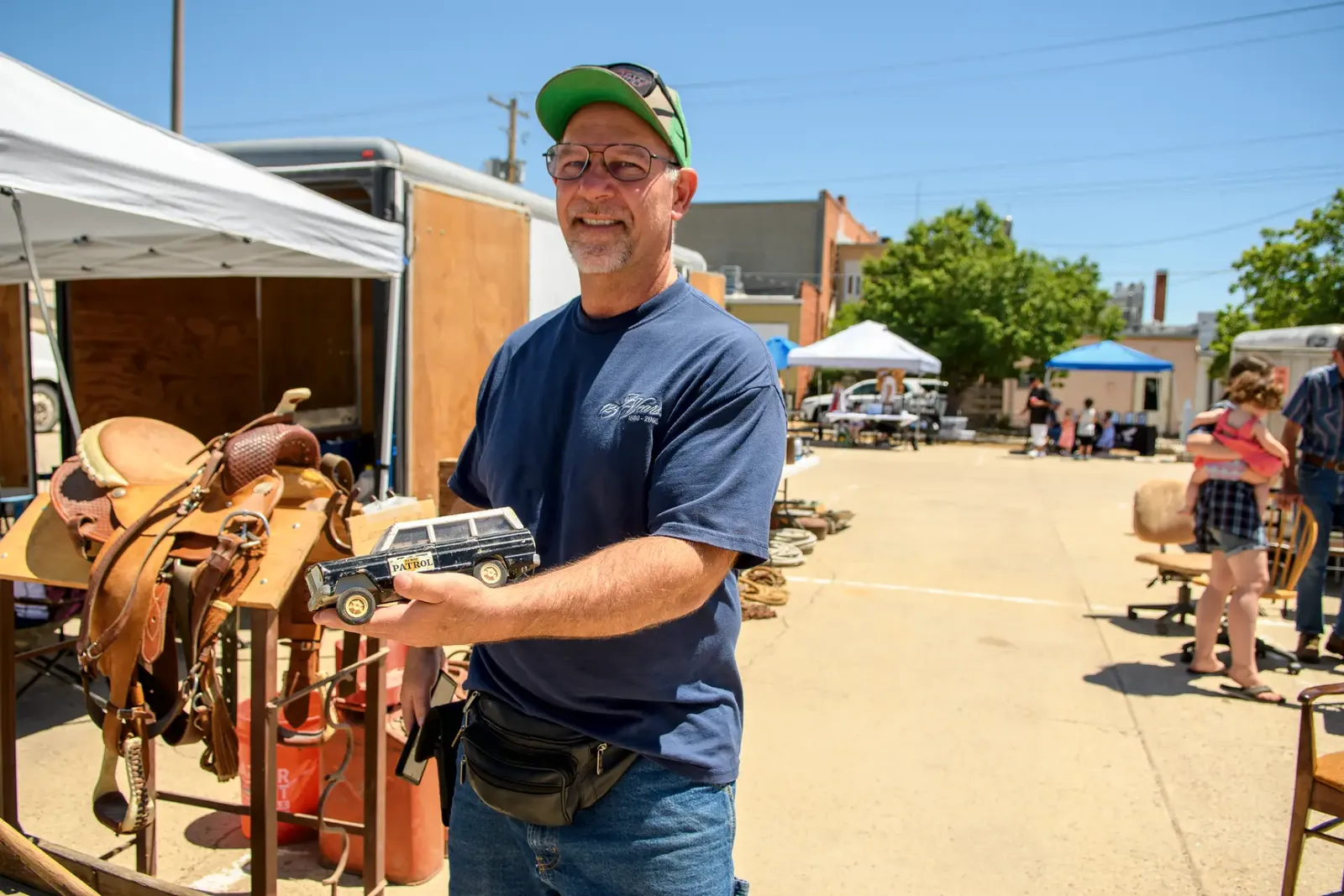 Vendor holding a vintage toy truck beside leather saddles