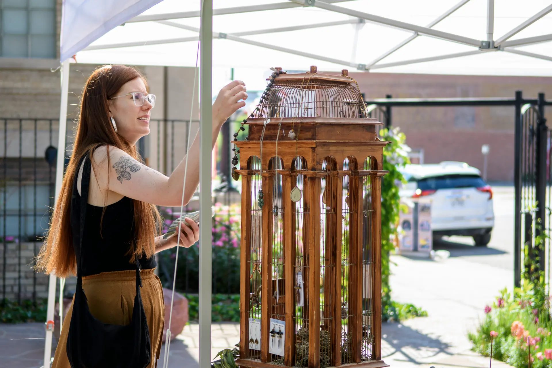 Vendor arranging necklaces on a tall wooden birdcage display under a white canopy