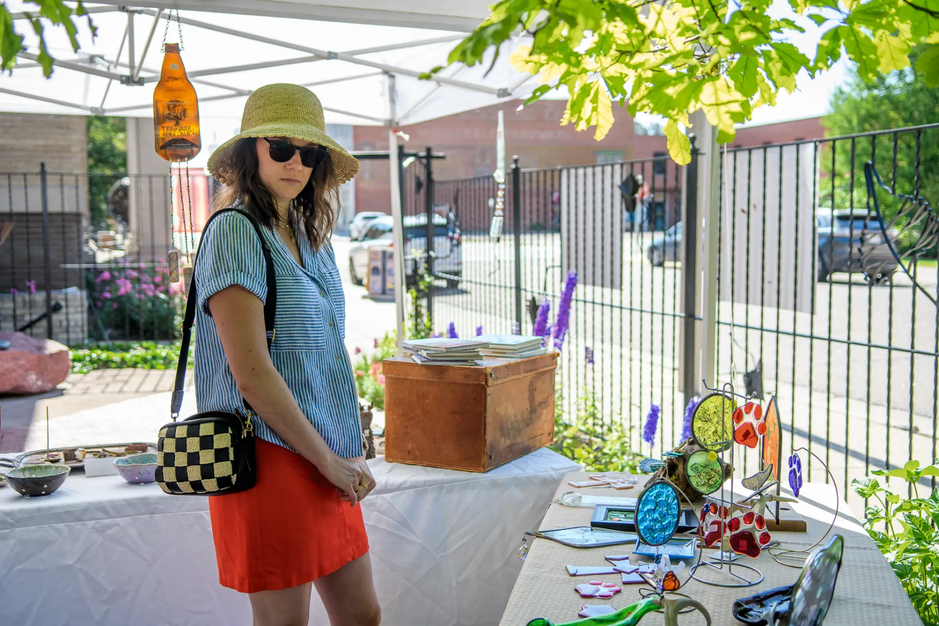 Shopper in a straw hat beside a table of stained glass and ceramic pieces