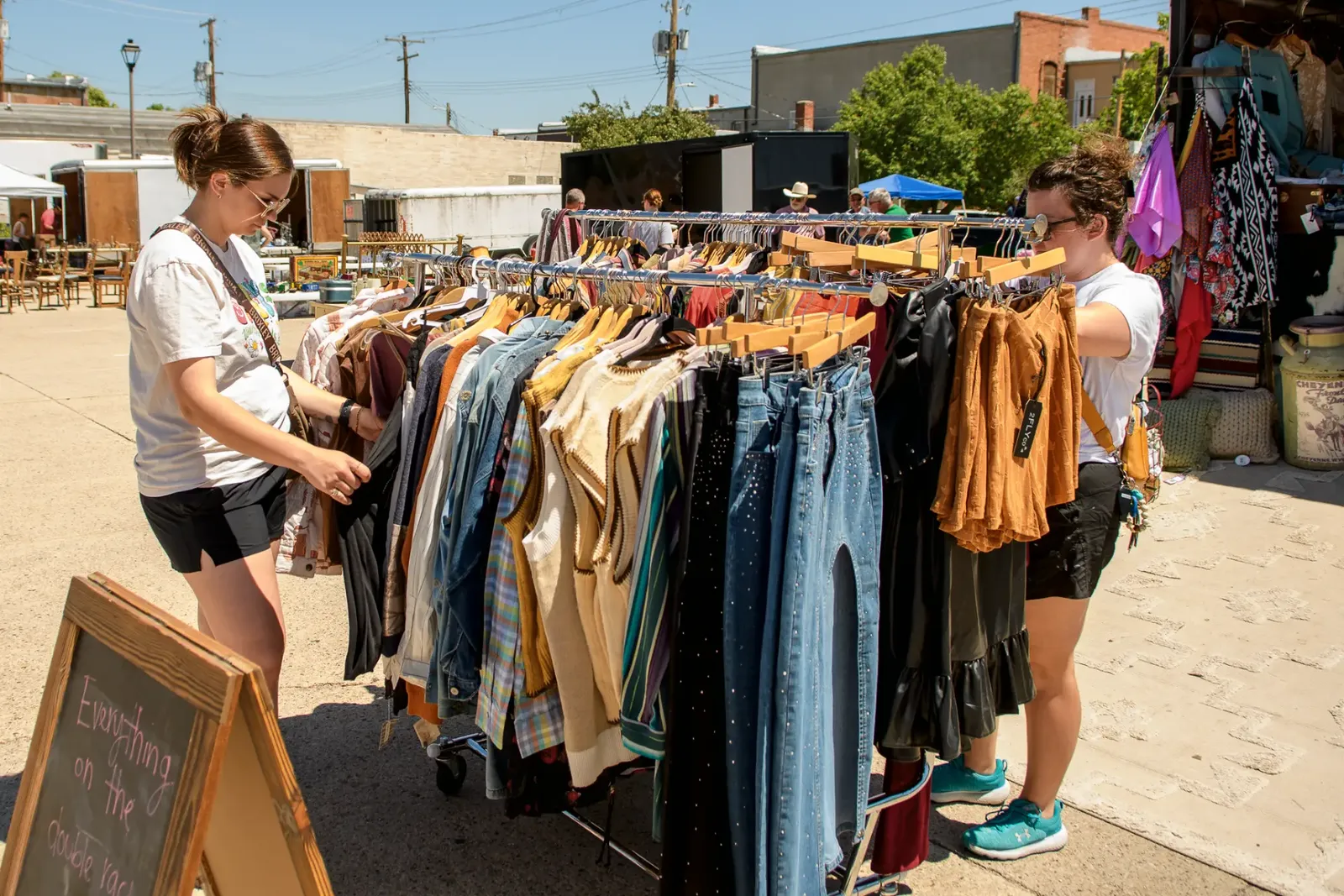 Two shoppers looking through a clothing rack beside a chalkboard sign